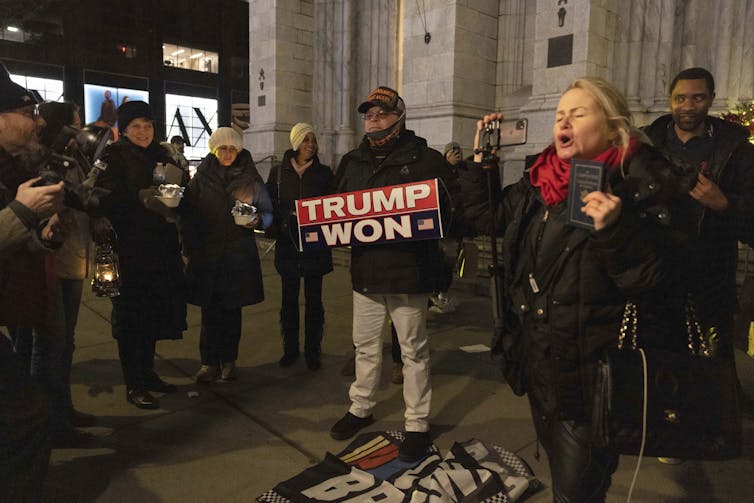 A small group of protesters in a circle, with a man holding a 'Trump won' poster in the middle.