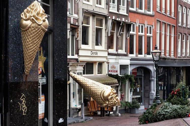 A gold ice-cream cone sculpture and christmas trees lie on the ground in a city centre street.