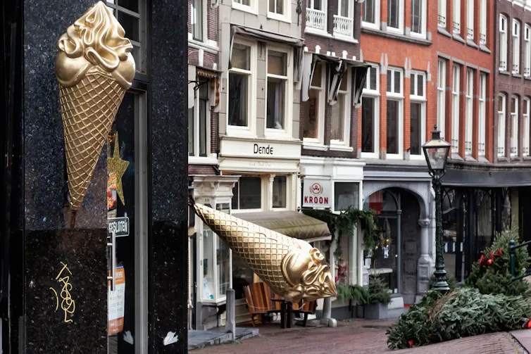 A gold ice-cream cone sculpture and christmas trees lie on the ground in a city centre street.