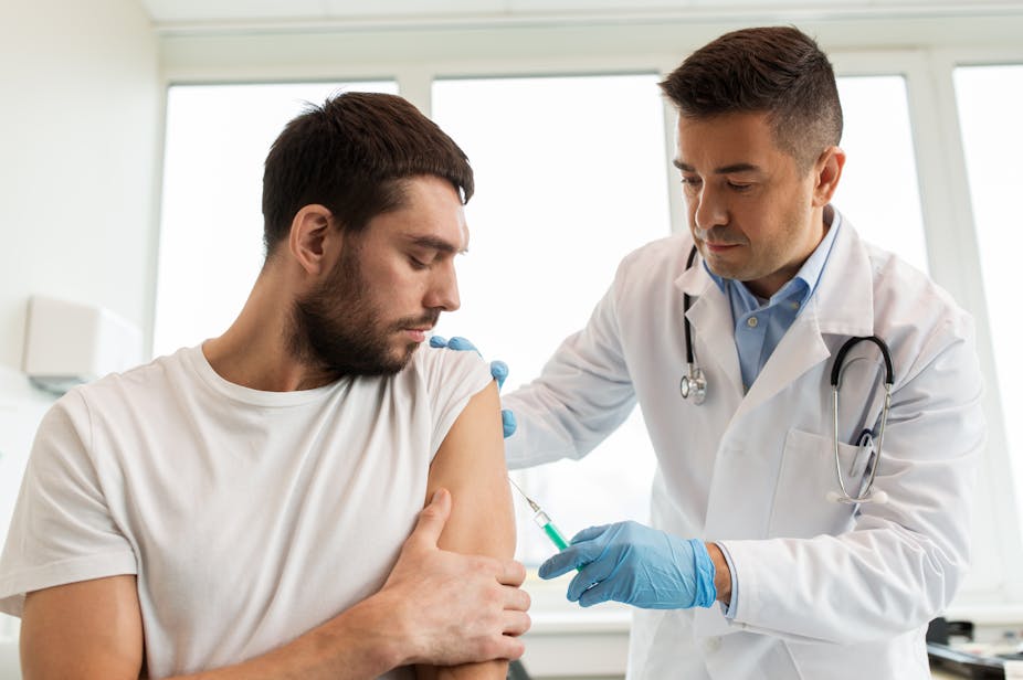 A young adult man receives a vaccine from his doctor.