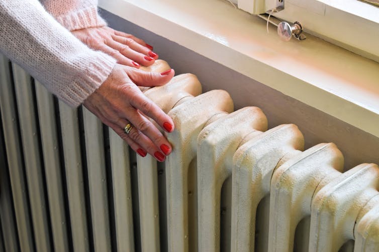 Close up photo of a woman's hands against an old-fashioned radiator