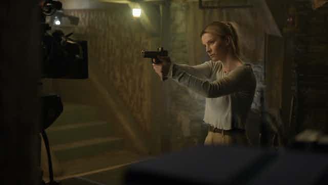 Una mujer empuñando una pistola apunta hacia una cámara de cine.