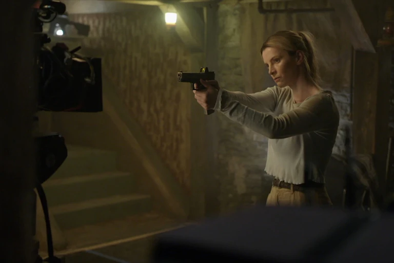 Una mujer empuñando una pistola apunta hacia una cámara de cine.