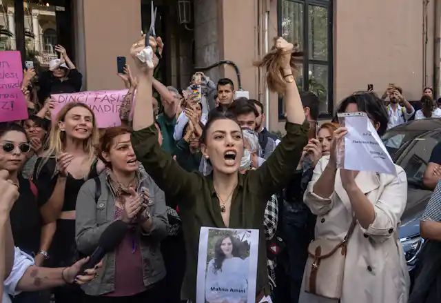 Woman shouting and holding up hair and scissors among group of clapping women