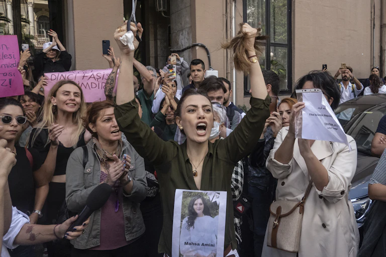 Woman shouting and holding up hair and scissors among group of clapping women