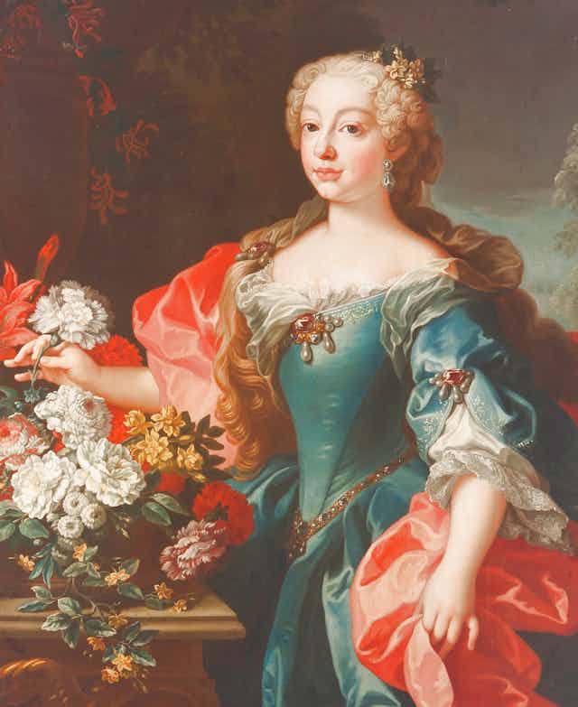 Una mujer vestida con amplios y lujosos ropajes posa de pie para un pintor.