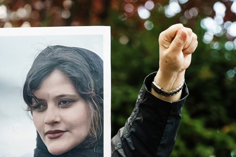 A clenched fist next to a picture of a young woman in a hijab.