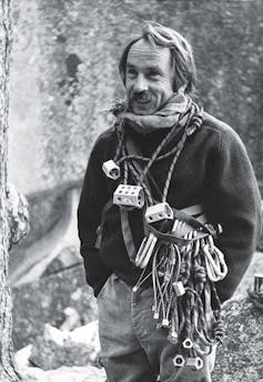 A black and white photo of a man wearing large numbers of rock climbing gadgets.