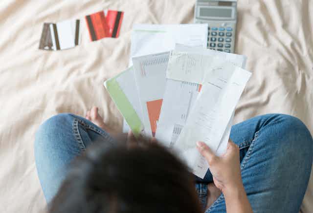 Top view of young woman sorting through bills on a bed