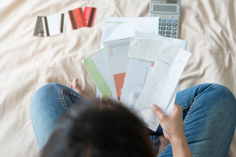 Top view of young woman sorting through bills on a bed