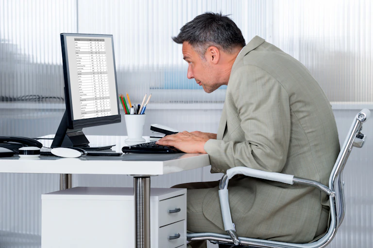 Un homme se tient tout voûté devant son ordinateur, à son bureau
