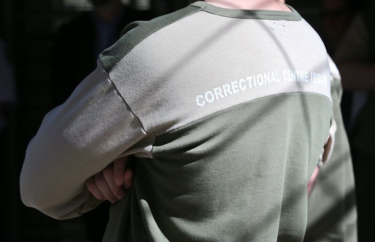 A man in prison clothes crosses his arms.
