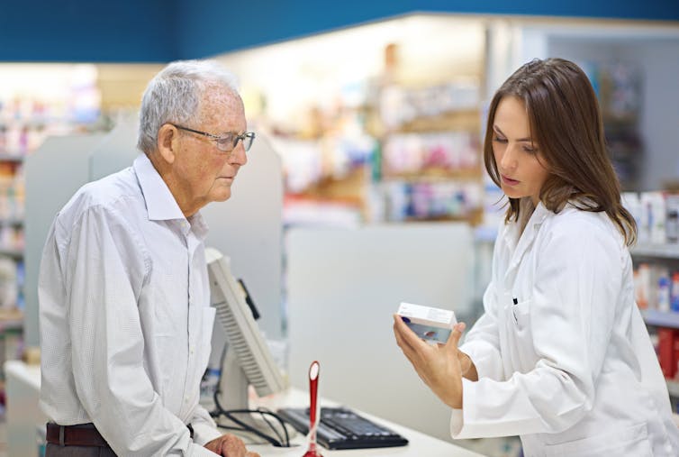 An elderly man talks to a young pharmacist about his prescription.