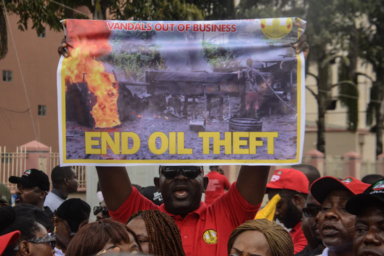 A man holds a banner proclaiming "END OIL THEFT"