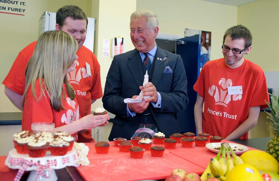 Prince Charles laughs while decorating cupcakes with there young people in red Prince's Trust t-shirts.