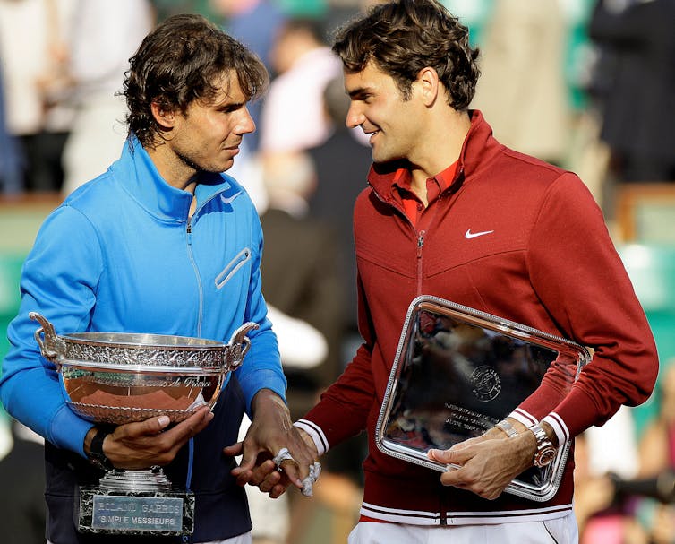Tennis players Roger Federer and Rafael Nadal laughing together on court after a match.