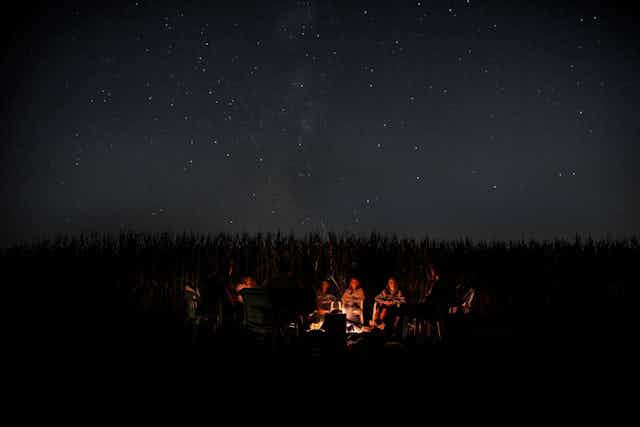 Un grupo de personas se reúne de noche alrededor de una hoguera.