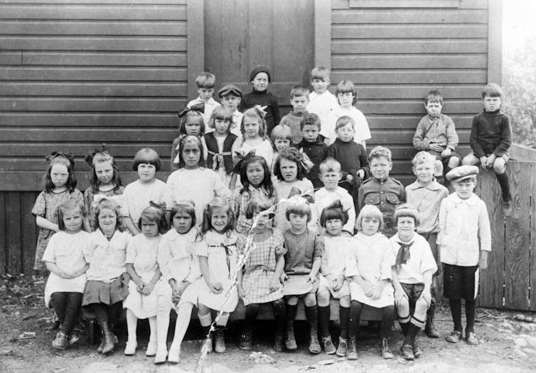 Black and white photo of children seen in rows in front of a school photo.