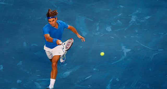 Roger Federer running for a shot on a blue court with a green ball.