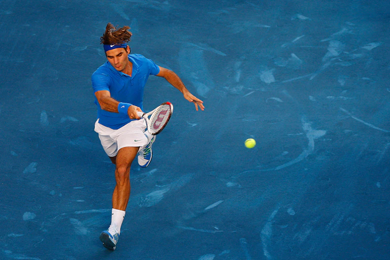 Roger Federer running for a shot on a blue court with a green ball.