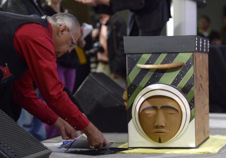 A man seen bending placing an item down in front of a carving on a wooden box.