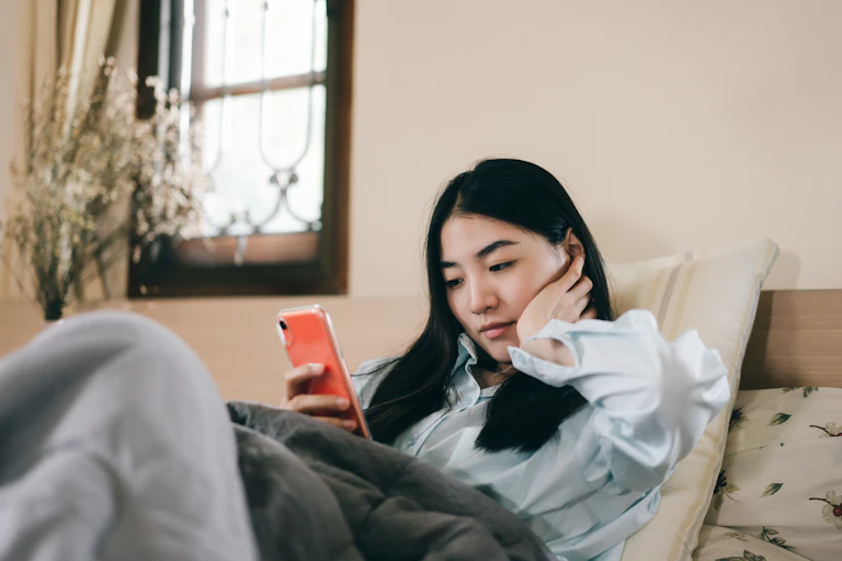 Jeune femme adulte célibataire utilisant un smartphone en matinée pour une application de technologie moderne pour la santé mentale à la maison.
