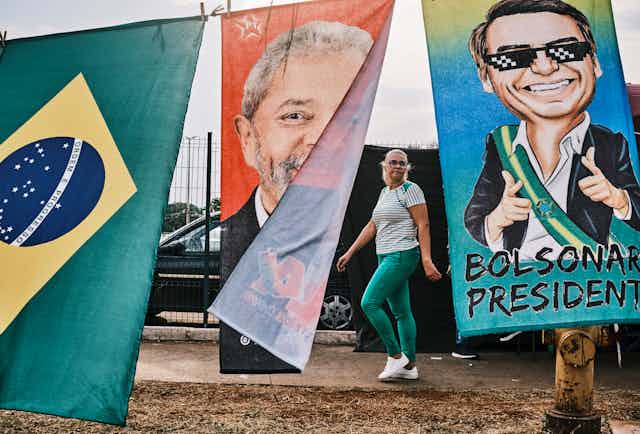 Fabric banner depicting Luiz Inacio Lula da Silva and Jair Bolsonaro flutter in the wind as a woman dressed in green and white looks on.