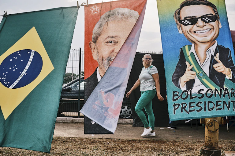 Fabric banner depicting Luiz Inacio Lula da Silva and Jair Bolsonaro flutter in the wind as a woman dressed in green and white looks on.