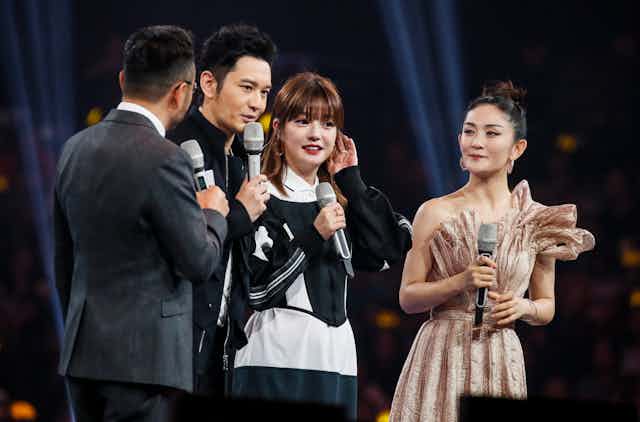 Four Chinese celebrities speak into microphones on stage.