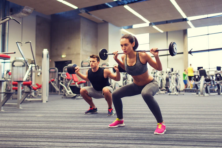A woman and a man lift lighter weights in a gym.