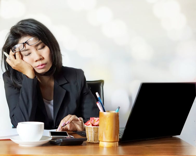 A person is sitting at their desk with a laptop, visibly tired.