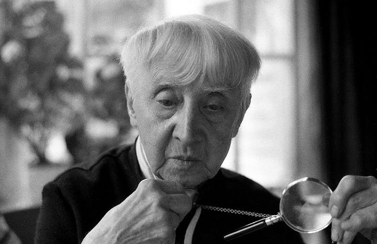 An older woman with cropped white hair peers at her glasses.