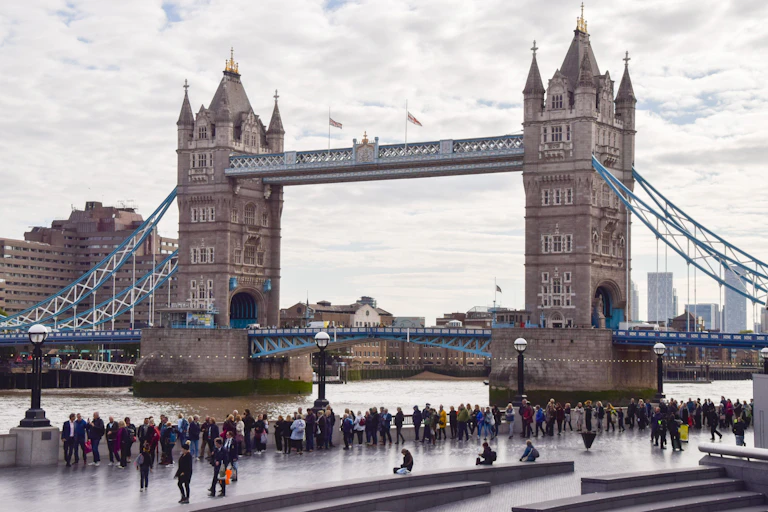 A bridge over a river with a queue of people on the river bank.