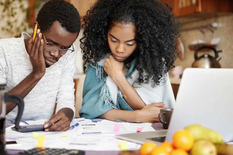 A young couple looking down at calculators, receipts and forms, discussing finances