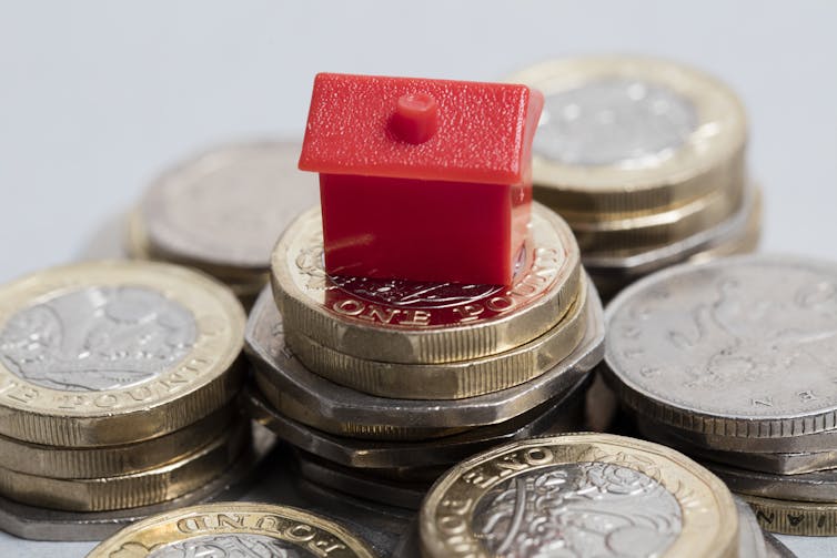 A red Monopoly house marker sitting on top of a pile of pound coins