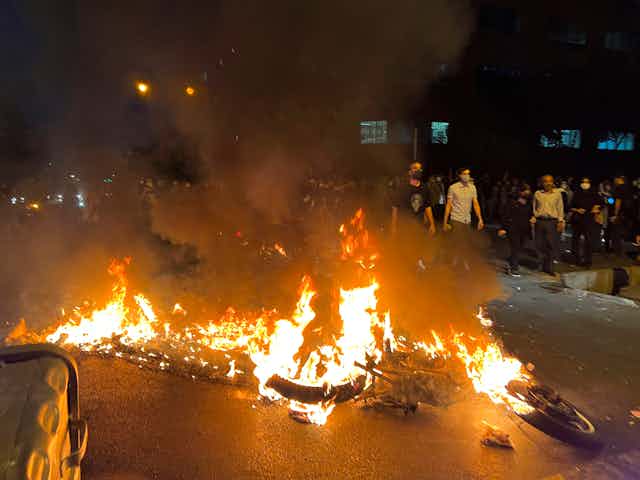 Flames from a burned police motorcycle at a night-time protest.