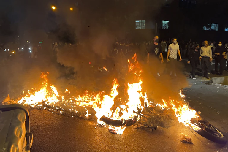 Flames from a burned police motorcycle at a night-time protest.