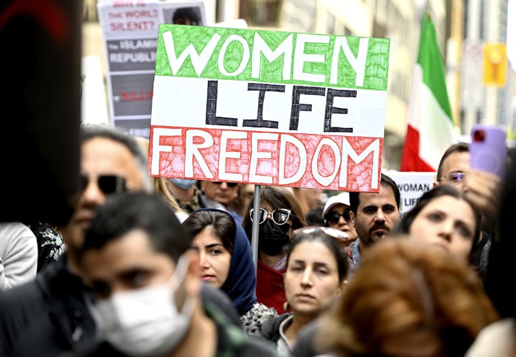 A woman holds a sign that reads Women, Life, Freedom at a protest march.