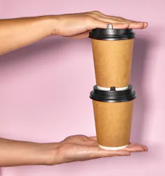 Hands seen holding two stacked cups of hot beverages.