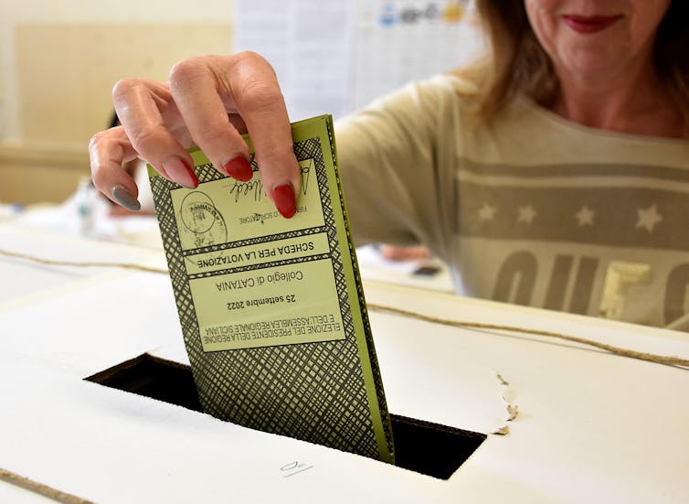 Close up of a woman's hand placing a ballot into a box