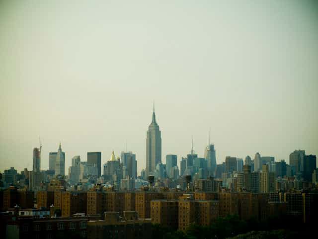 Delante de la silueta de Manhattan y el Empire State se ven una serie de edificios de viviendas sociales de ladrillo marrón.