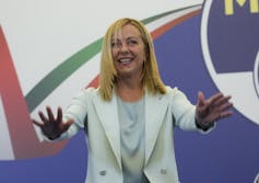 A woman in a white suit waves.
