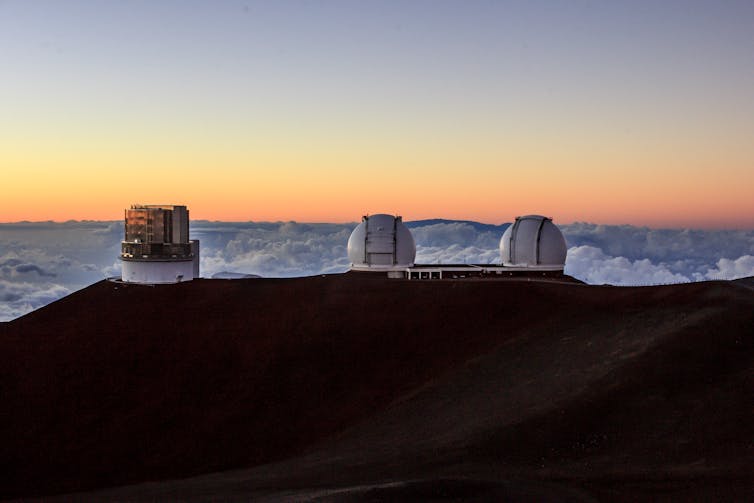 Three telescopes on a mountain top, sitting above the clouds