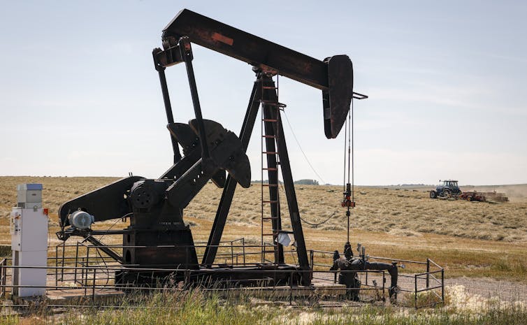 An oil pumpjack sits in the foreground of a large hay field
