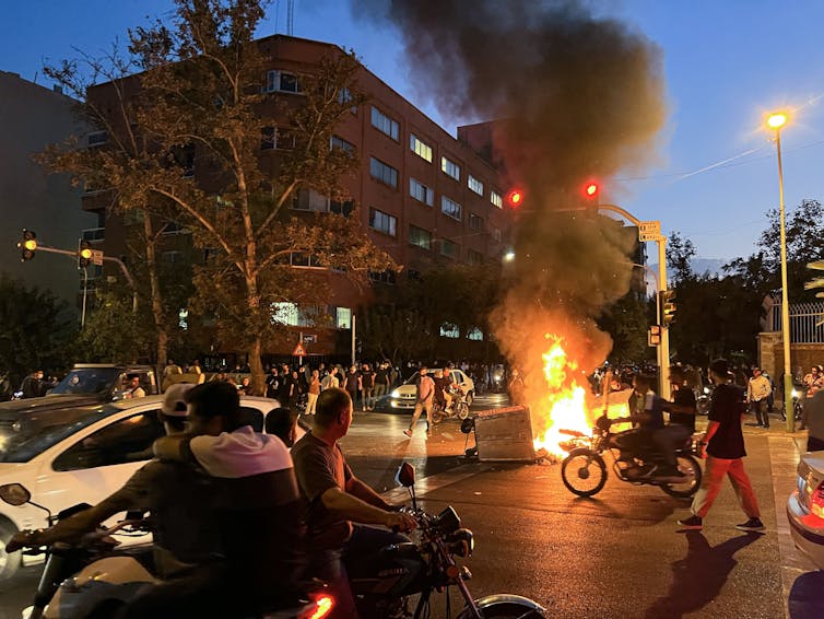 Un incendio arde en medio de una calle en Irán mientras cientos de personas se reúnen.