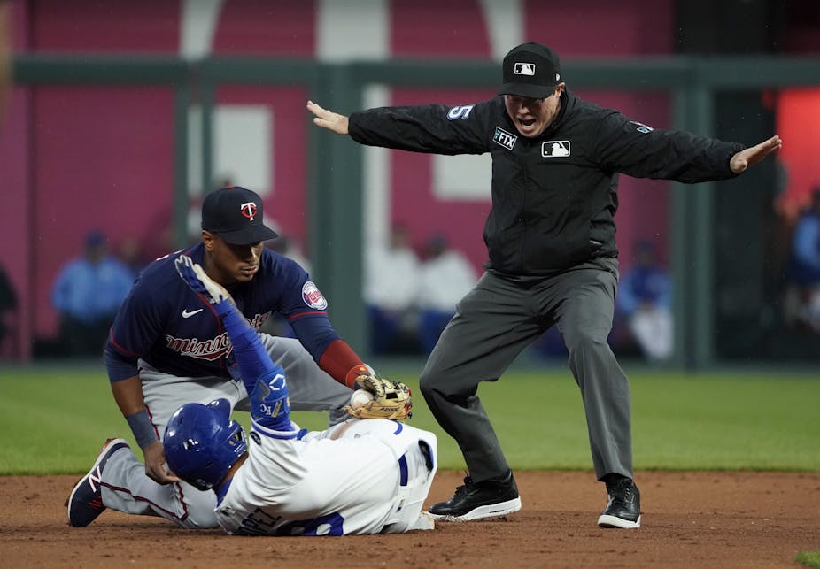 a baseball player slides apparently evading a tag while an umpire makes the call