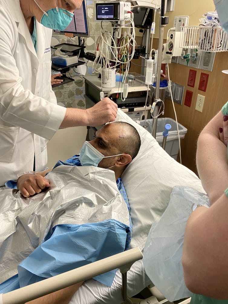 A neurosurgeon prepares his patient, who is lying down, for deep brain stimulation surgery.