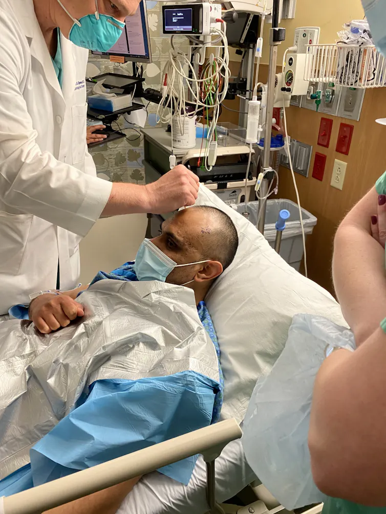 A neurosurgeon prepares his patient, who is lying down, for deep brain stimulation surgery.