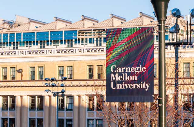 A sign on a lamp post reads Carnegie mellon university. A beige building in the background.