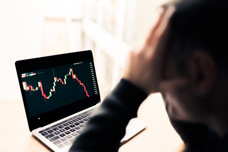 Person with head in hand looking at laptop with downward trending graph